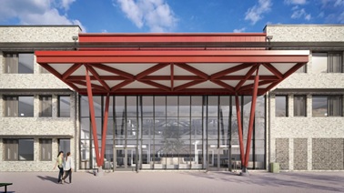 caledonia-1.png Front entrance of a modern school building with a wide glass façade. A large red steel canopy with triangular beams projects outward above the doors, supported by angled columns. Light‑coloured brick walls with rows of windows frame the entrance. Two people walk across an open paved area in front. The sky is blue with scattered clouds, and benches and bins sit near the entrance.