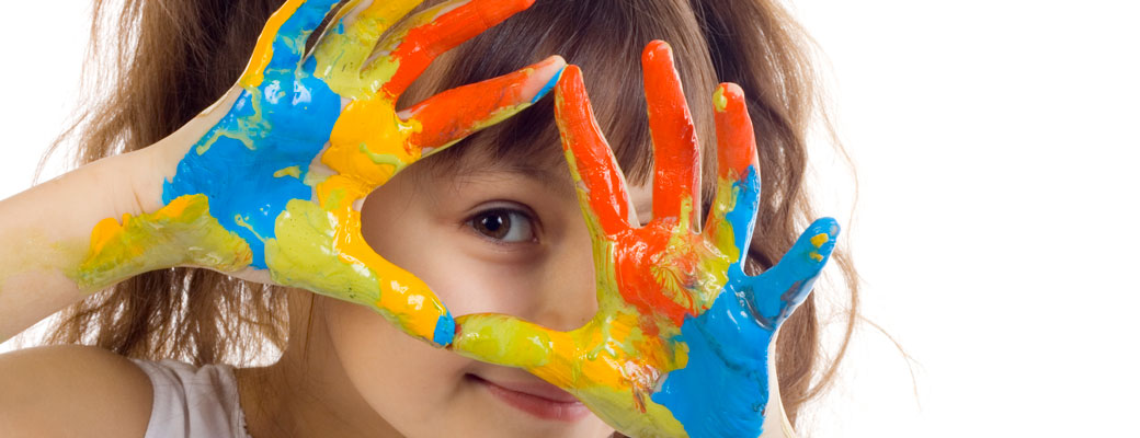 girl looking through her hands that are covered in colourful paint
